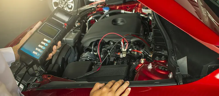 Diagnosegerät wird am Motorraum eines roten Fahrzeugs angeschlossen