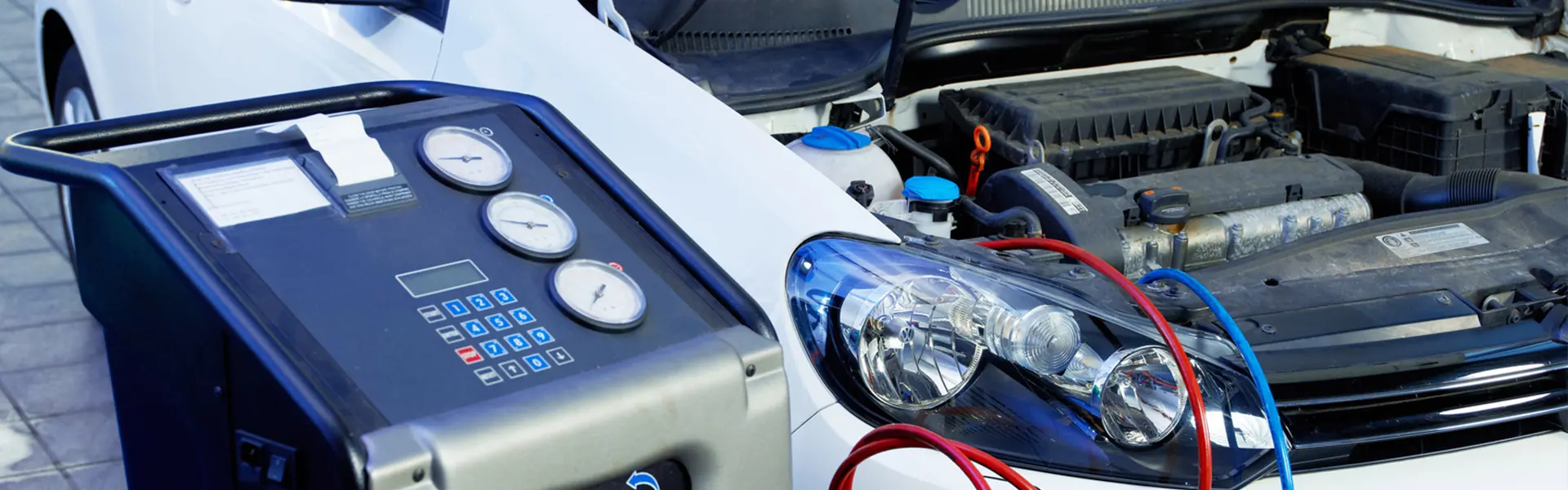 Klimaservicegerät mit Messuhren steht am geöffneten Motorraum eines Fahrzeugs
