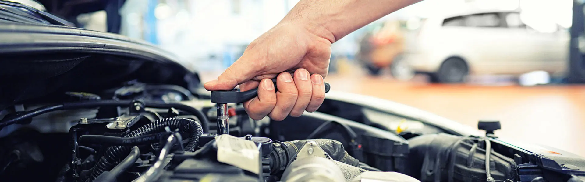 Mechaniker arbeitet mit Ratsche am geöffneten Motorraum eines Fahrzeugs