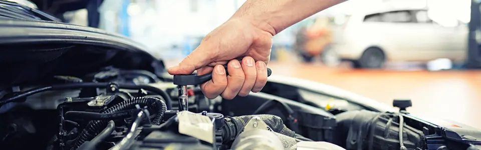 Mechaniker arbeitet mit Ratsche am geöffneten Motorraum eines Fahrzeugs